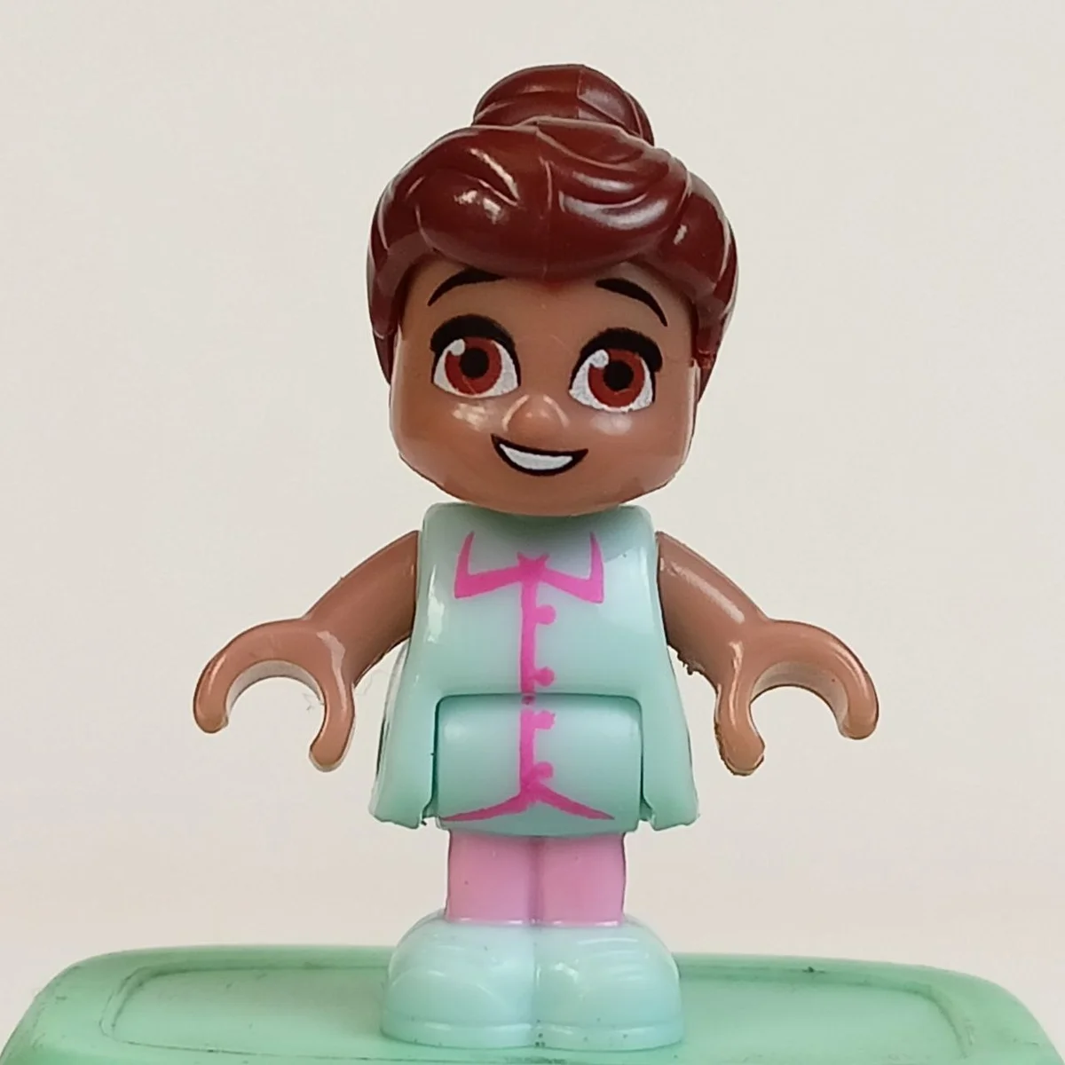 Yootz figure, female, light brown skin, brown bun hair, brown eyes, light sky blue shirt with barbie pink buttons and coral, light pink pants