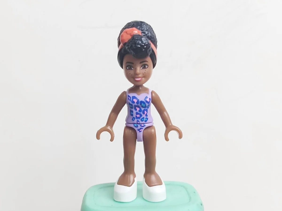 Barbie Micro-Doll medium brown skin, lavender swiumsuit with dark blue, pink and azure leopard pattern, black feza hair with coral bandana, dark brown eyes,  white slippers